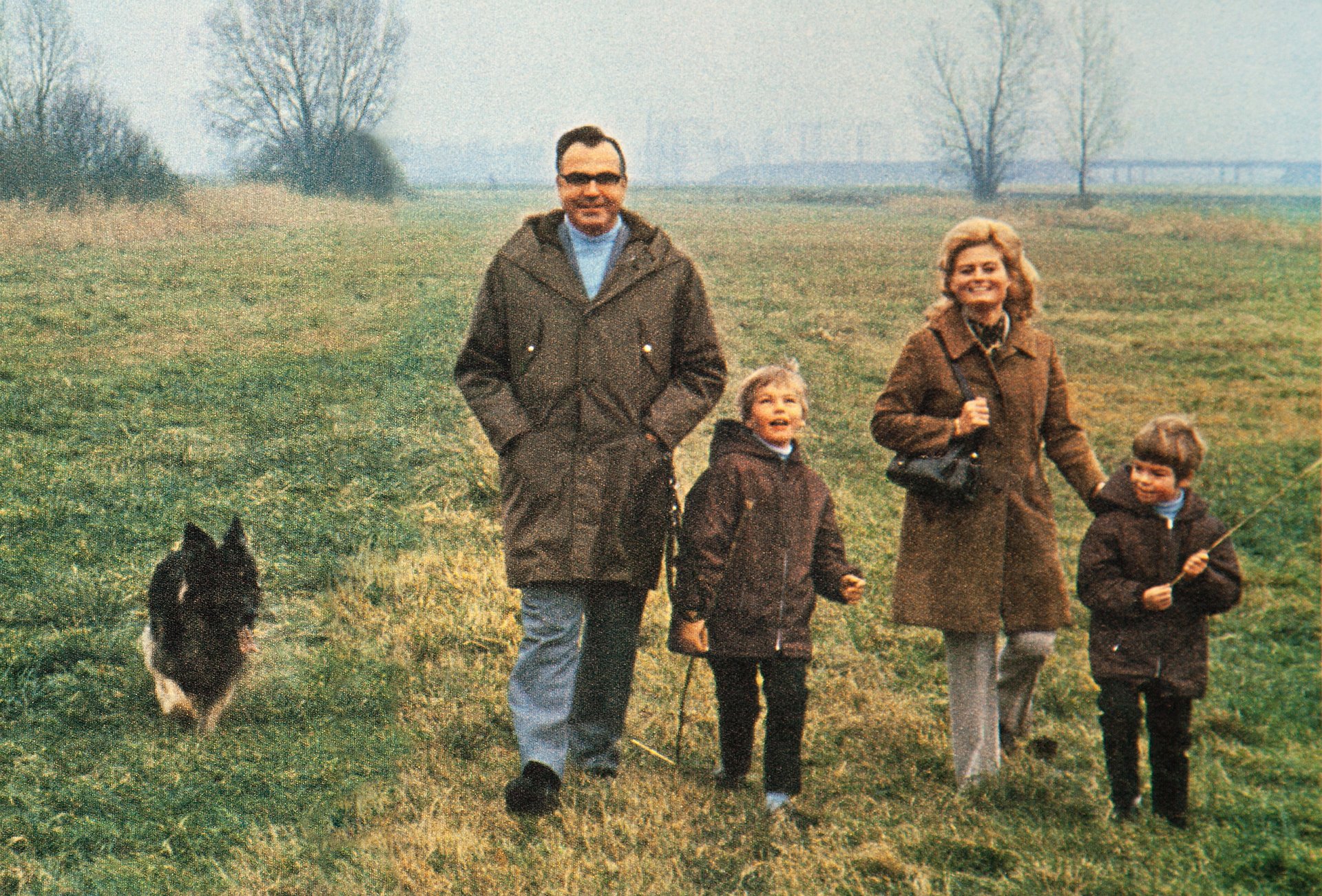 Herr und Frau Kohl gehen mit ihren zwei Kindern auf einer Wiese spazieren