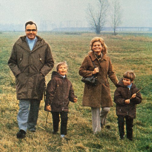 Herr und Frau Kohl gehen mit ihren zwei Kindern auf einer Wiese spazieren