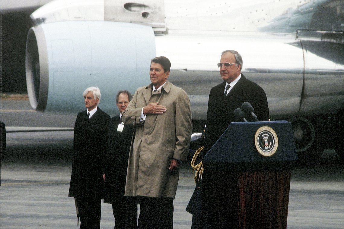 Kohl und Reagan stehen auf einem Flugfeld an einem Rednerpult