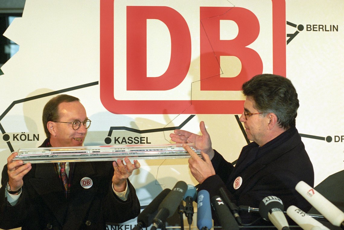 Aufnahme von Heinz Dürr und Matthias Wissmann mit einer Modelleisenbahn vor dem Logo der Deutschen Bahn
