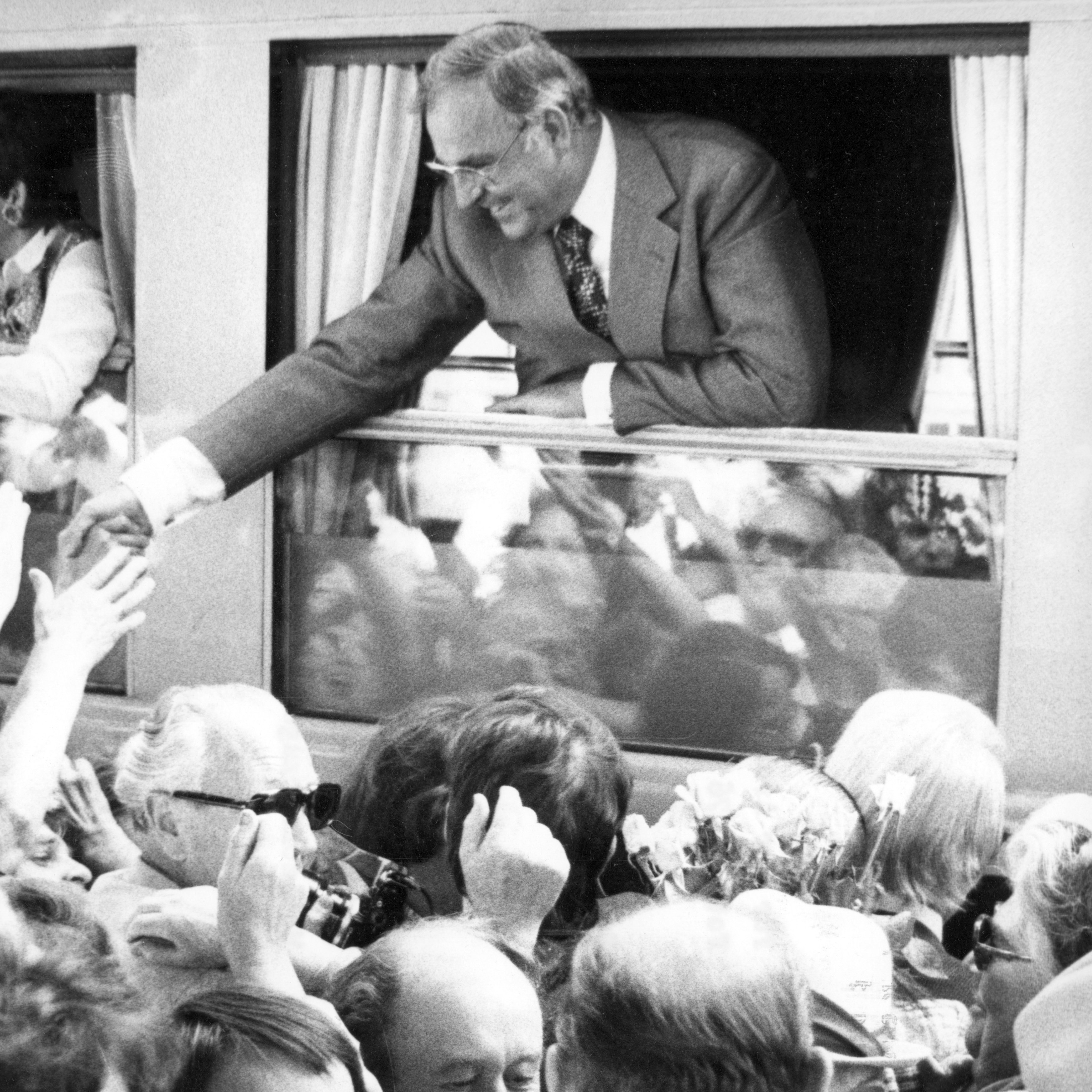 Schwarz-Weiss-Aufnahme von Helmut Kohl beim Grüßen umstehender Menschen aus einem Zugfenster