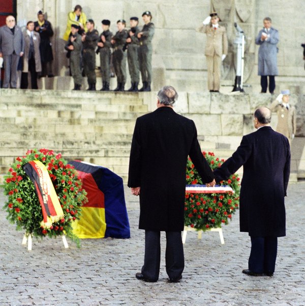 Aufnahme von Helmut Kohl und François Mitterrand Hand in Hand vor Blumenkränzen